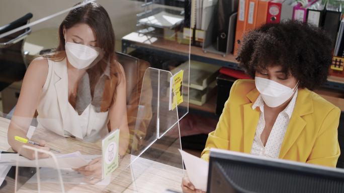 与2019冠状病毒疾病的快乐与新常态办公室合作，女商人与同事穿过屏幕隔板以避免2019冠状病毒疾病大