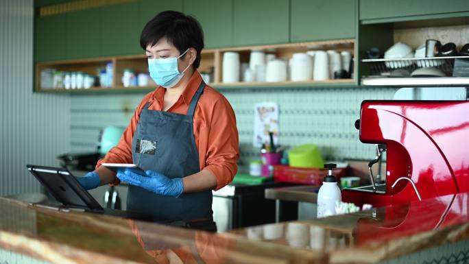 一位戴着口罩和防护手套的亚裔中国小企业主输入结账付款