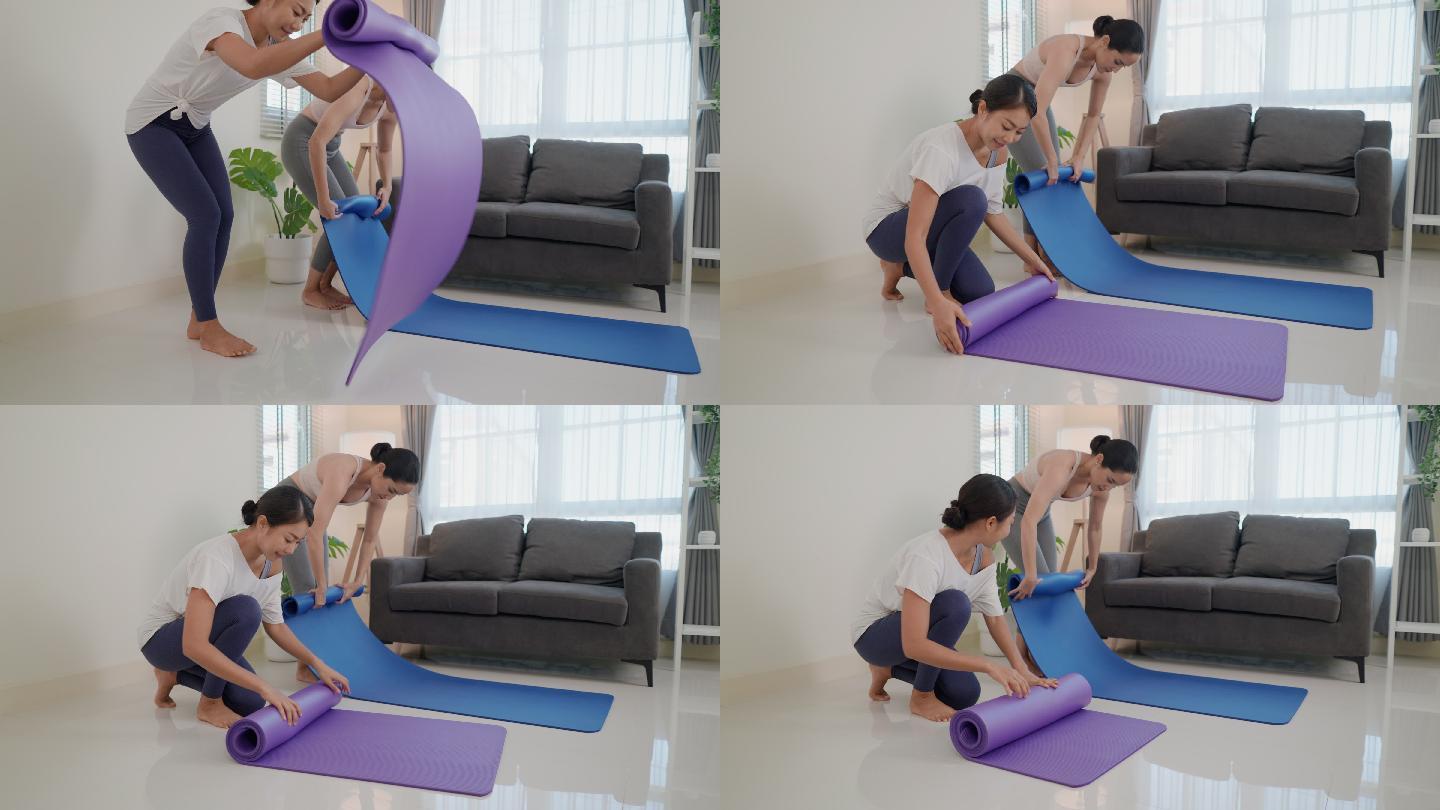 两位年轻迷人的亚洲女性在家锻炼完后，叠起紫色和蓝色瑜伽垫或健身垫。健康、健康生活和日常生活中的健康活