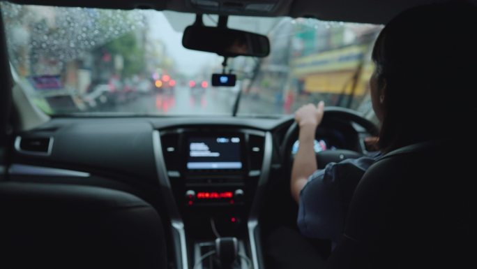 亚洲女性下班开车回家时，倾盆大雨。