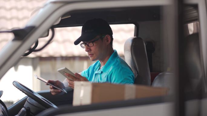 亚裔中国成熟男性送货员在送货车司机座上用电话与客户沟通