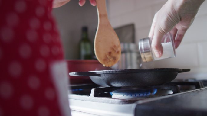 一个面目全非的女人正在家里厨房里煎的食物里加盐