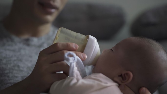 周末，亚裔中国年轻父亲在客厅用奶瓶喂养男婴