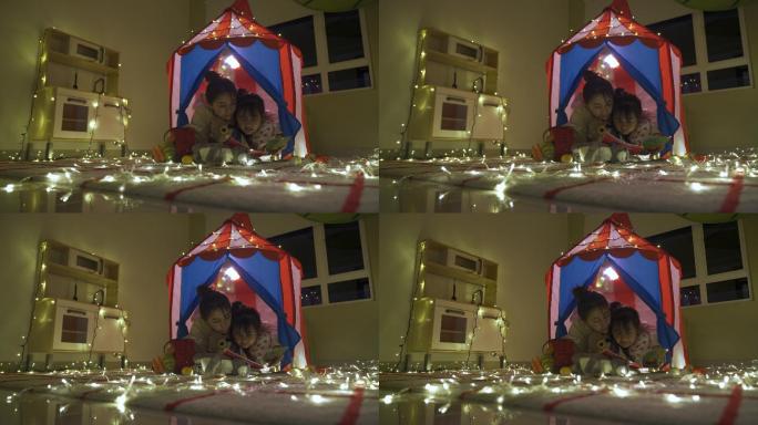 亚裔中国妈妈在家里一个温暖明亮的帐篷里给女儿读故事