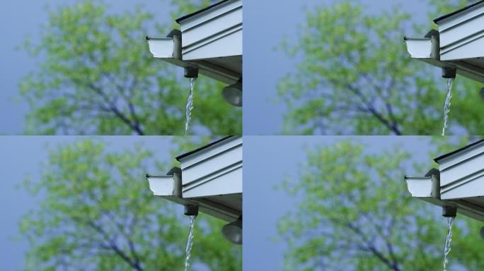 从排水沟沿屋檐倾泻而下的雨水的慢镜头，背景是树木
