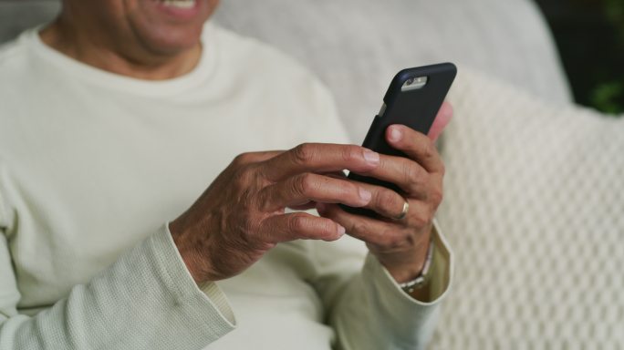 一名老人独自坐在家里的沙发上，使用手机的4k视频片段