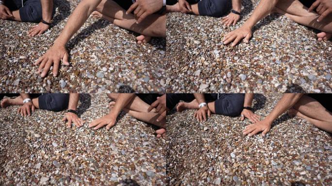 特写：两个朋友在海滩上用手抚平卵石。