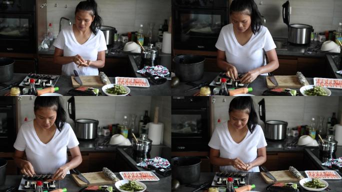 一名泰国妇女用寿司米饭和虾制作尼吉里卷，并将其与基本寿司卷一起放在盘子上