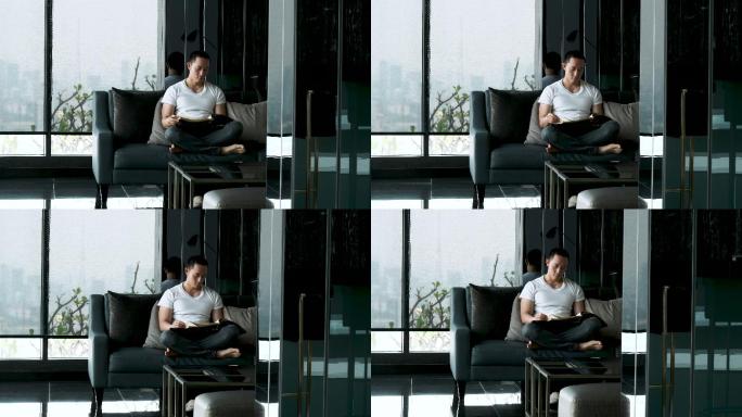 英俊的亚洲男人下班后在家里的沙发上看书