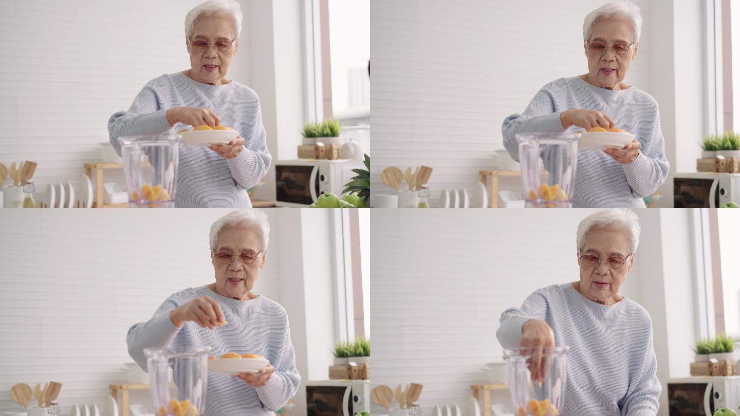 亚洲老年女性，80岁，用电动搅拌机自己添加橘子来准备水果冰沙，享受健康饮食、正面视图、城市生活中的老