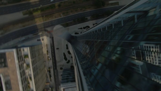 反射蓝天的玻璃摩天大楼。FPV无人机以圆周运动沿建筑物向下移动