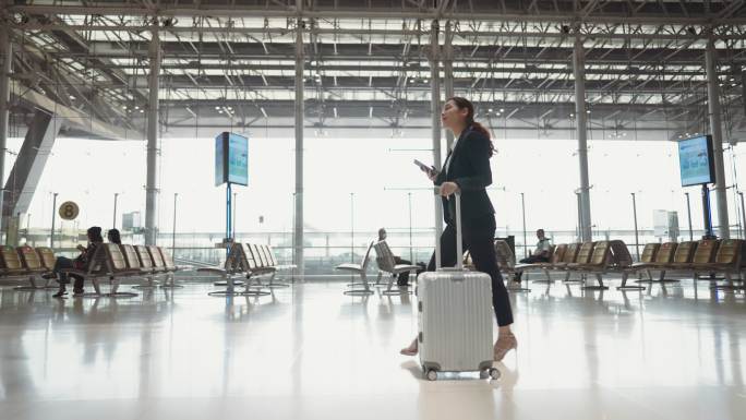 年轻女商人在使用智能手机时穿过机场航站楼