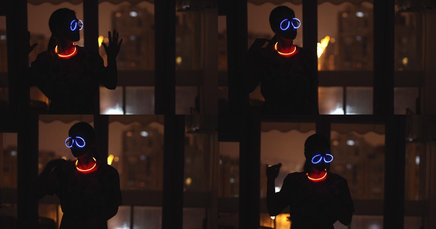 戴着霓虹眼镜和手镯的女人在窗户前的暗室里跳舞