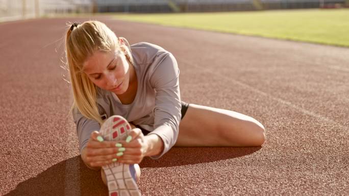 SLO MO女运动员坐在体育场跑道上伸展双腿