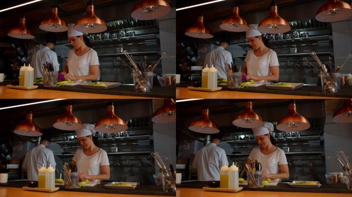 女副厨师长在切菜，而主厨在一家grommet餐厅的后台工作