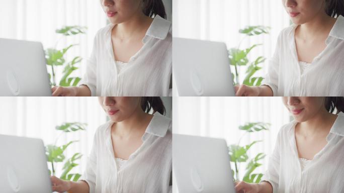 一位年轻的亚洲女性坐在客厅的沙发上用笔记本电脑工作的特写镜头。