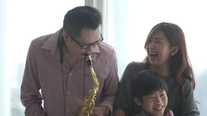 亚裔中国父亲喜欢在周末闲暇时间和家人在家吹萨克斯管