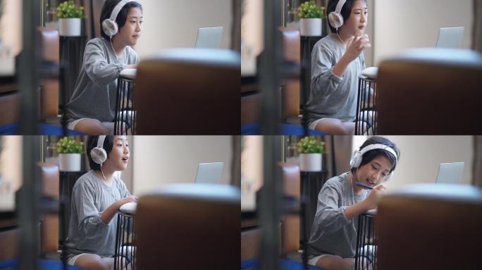 亚洲青少年在起居室通过数字远程设备笔记本电脑网络会议从学校老师那里学习电子学习在线课程，亚洲青少年在