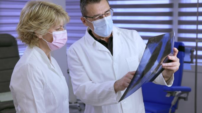 医生和他的女同事戴着防护面罩，检查X光片