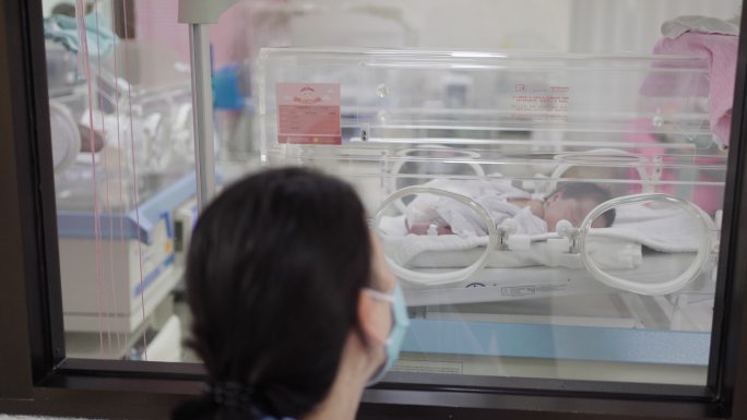 在医院里，母亲用爱和关怀看着保育箱中的婴儿。