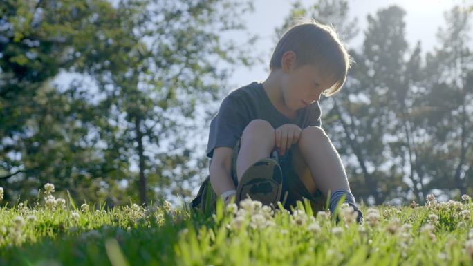 7岁的男孩坐在公园的绿草上，享受着美丽的大自然。