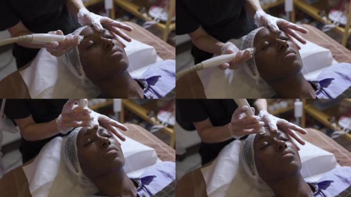 放松的年轻漂亮黑人女子在水疗中心接受面部护理