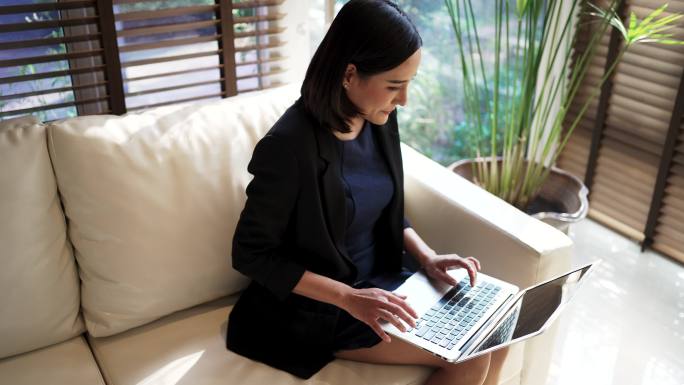 亚洲女商人在明亮的休息区使用笔记本电脑。