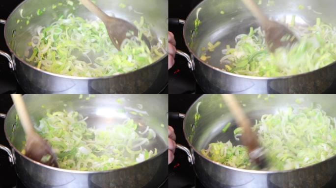 在大型不锈钢锅中炸切好的韭菜，用木勺搅拌