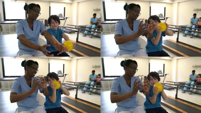 黑人友好治疗师向小男孩解释运动，小男孩在理疗时拿着球跟着她