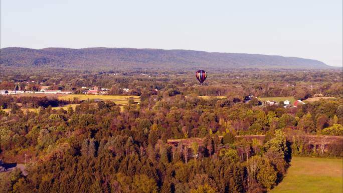 初秋的一个阳光明媚的夜晚，热气球正飞越美国宾夕法尼亚州波科诺斯的利海山谷。具有向后平移电影摄影机运动