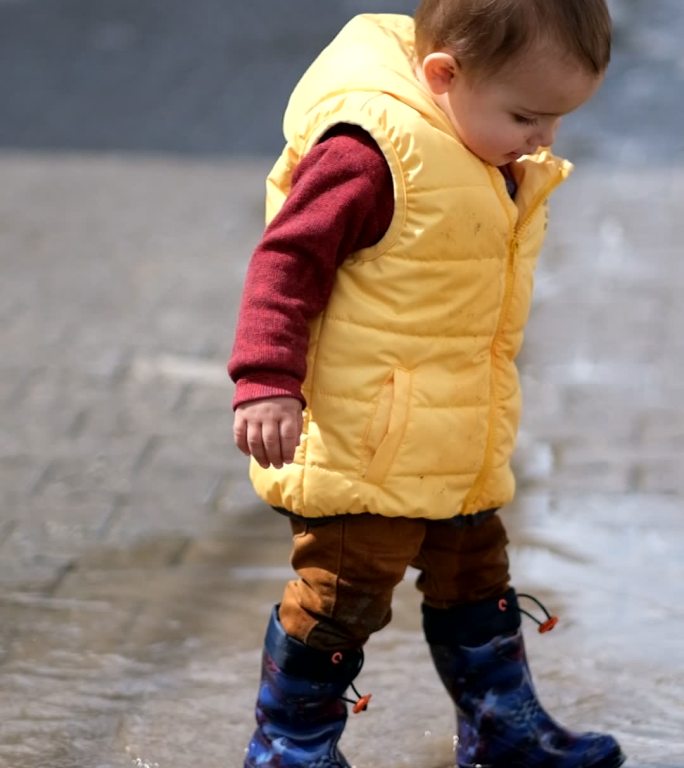 一个蹒跚学步的男孩喜欢在春天的一天在外面的水坑里玩耍