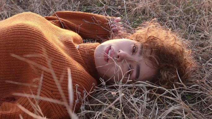 一位美丽的年轻女子躺在草地上叹气，享受着日落的温暖。