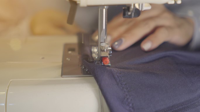 女性手拿牛仔布在缝纫机上，特写。服装维修、回收、家庭爱好和在家工作的概念。
