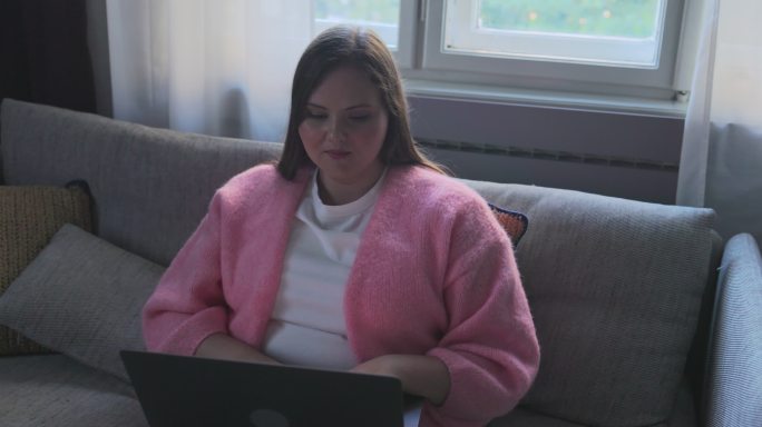 美丽的胖女人坐在客厅的沙发上，用笔记本电脑浏览网页