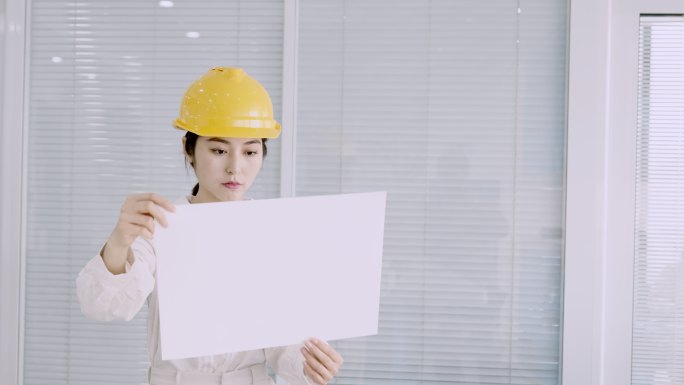 戴着黄色头盔的年轻漂亮的亚洲女工程师查看设计图纸