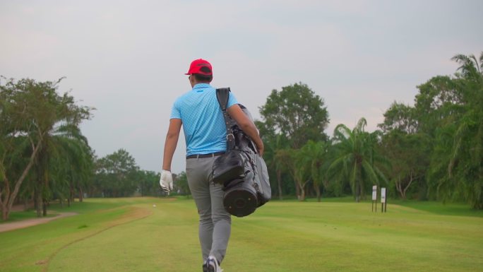 一名亚洲男子高尔夫球手在高尔夫俱乐部散步并携带高尔夫球袋