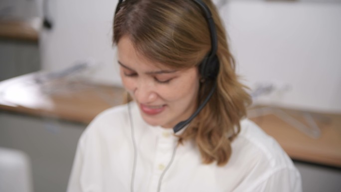 POV：微笑的亚洲女性，戴着耳机，使用笔记本电脑，在办公室与客户支持服务运营商交谈