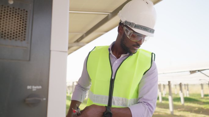 在太阳能农场，非洲年轻工程师穿着防护服，戴着安全眼镜和头盔，通过无线电与团队进行沟通