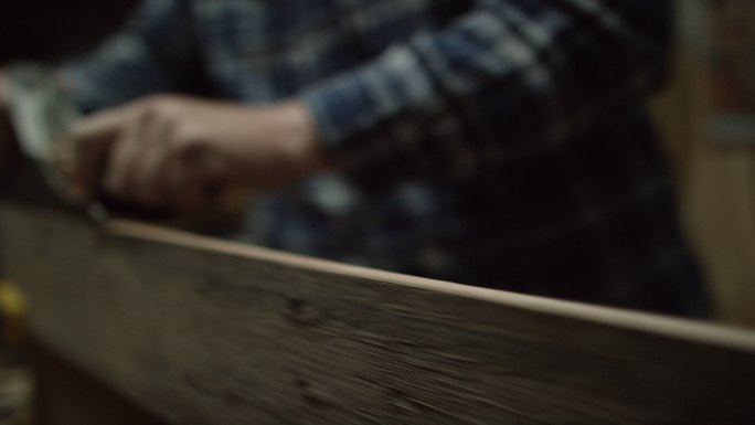 一位身穿格子衬衫的白人男性木工在红橡木板边缘使用5号复古手工刨子刨出木屑