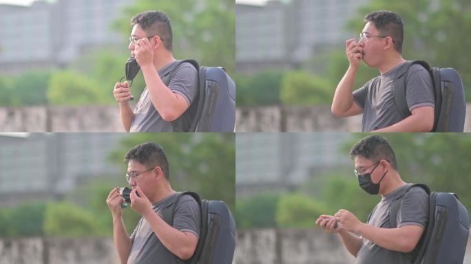 亚洲中国中年男子，戴着口罩，日落时在户外使用哮喘吸入器，背着乞丐