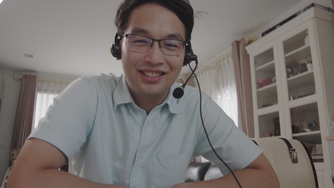 特写镜头：一名亚洲男子面带微笑地看着摄像机，在家里进行视频通话。