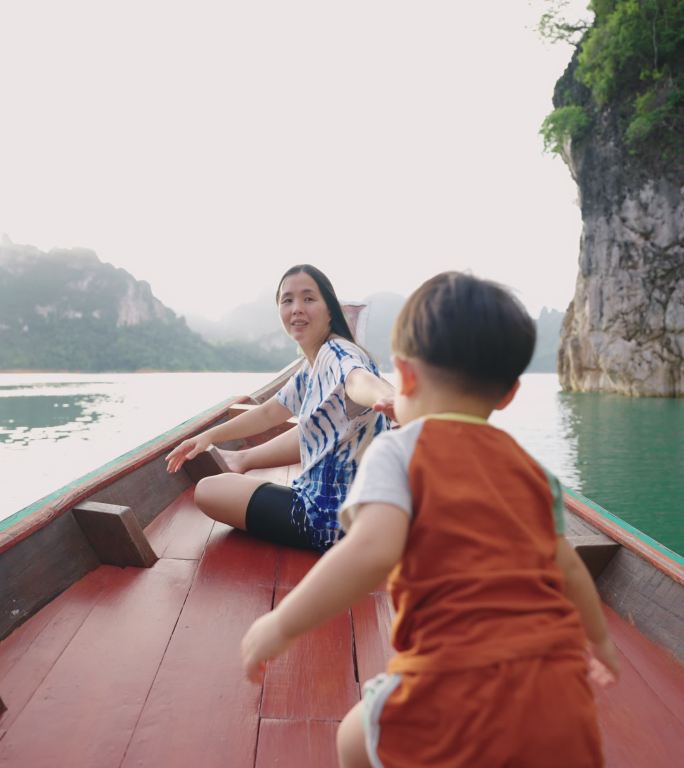 泰国南部，一对亚洲母子坐在一艘木制长尾船上，探索石灰岩悬崖和荒芜的海滩