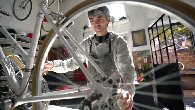 一位中年男子在一家自行车修理店修理自行车并转动后轮，看起来很专注