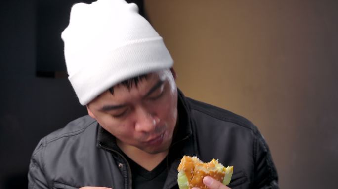 4K镜头青少年穿着冬衣，他拿着鱼汉堡，吃着美味的鱼汉堡。