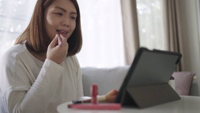 家里客厅里，女人在数码平板电脑上学习化妆，自己化妆