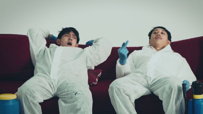 两名身穿2019冠状病毒疾病防护服的男性专家坐在沙发上休息。