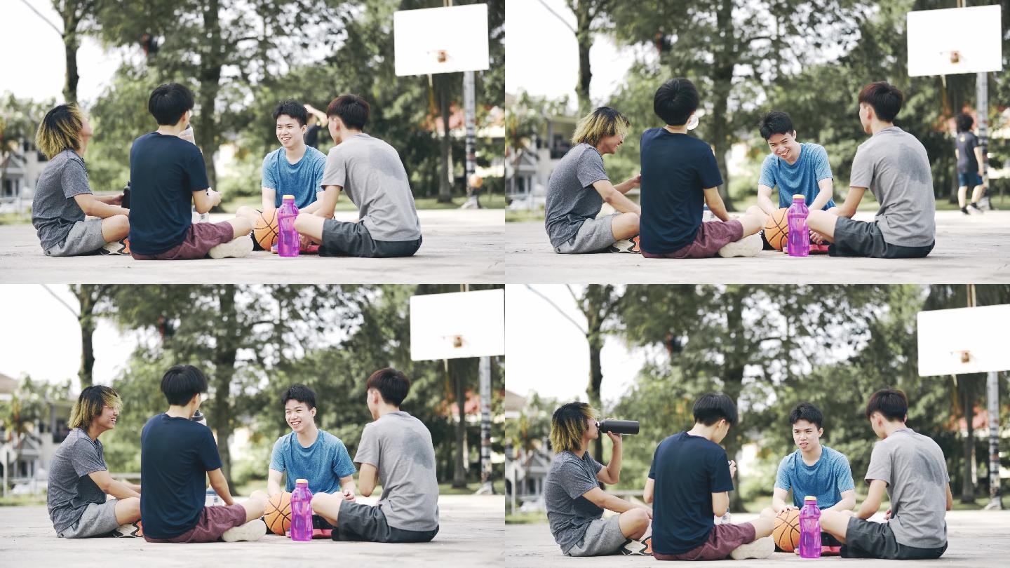 亚裔中国少年篮球运动员赛后与朋友坐在地上休息时喝水