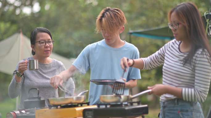 亚洲华人兄弟姐妹早上在露营时为家人准备早餐