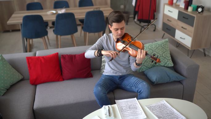 男小提琴家在家沙发上排练乐曲
