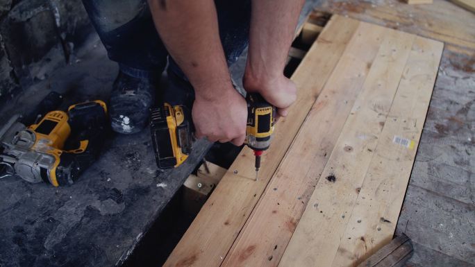 男性建筑工人使用电钻安装地板